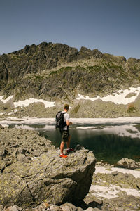 Man standing on rock by mountain against sky