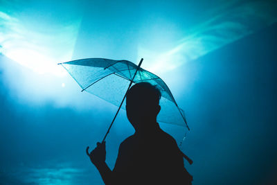 Rear view of silhouette woman holding umbrella against blue sky