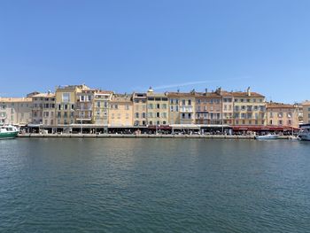 Buildings by sea against clear blue sky