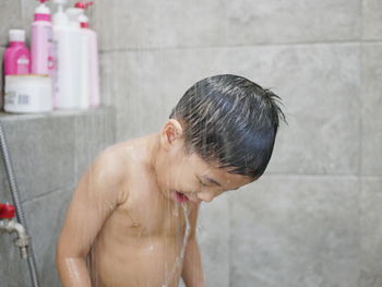 Shirtless boy bathing under shower in bathroom