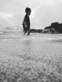 Boy playing on sand at beach against sky