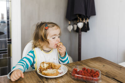 Girl eating food while sitting on table at home