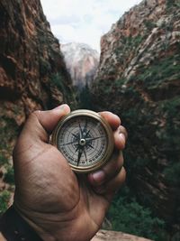 Cropped hand holding navigational compass against mountain