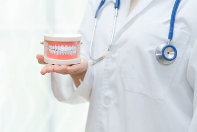 Midsection of doctor holding dentures