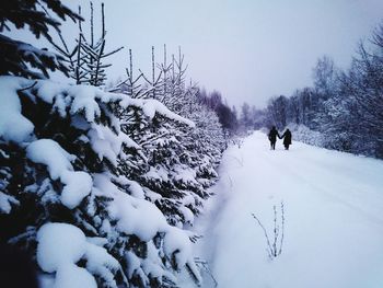 People walking on snow field against sky during winter