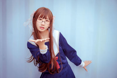 Portrait of young woman gesturing while standing against blue background