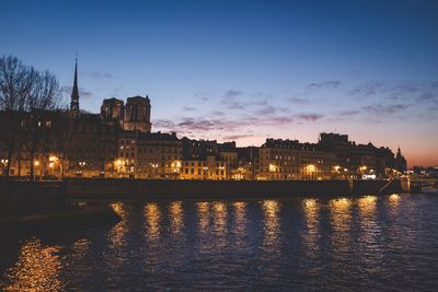 River by illuminated buildings against sky at sunset