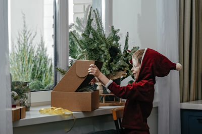 A thoughtful boy in a santa costume sits at the window and unpacking gifts