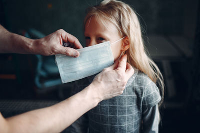 Cropped hand wearing mask to girl at home