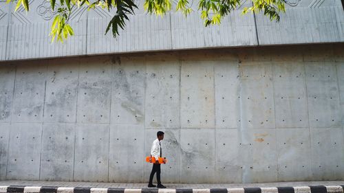 Full length of boy walking on footpath against wall