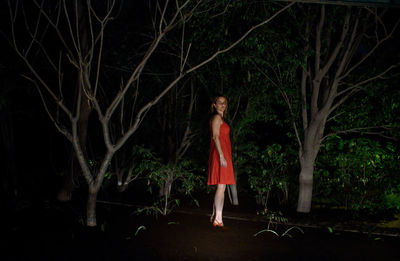 Full length of woman standing by trees in garden at night