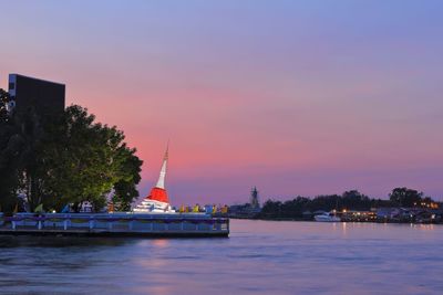 Scenic view of river by illuminated buildings against sky at sunset