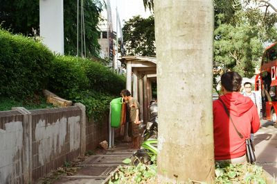 Rear view of people walking on street amidst trees in city