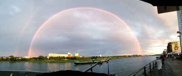 Scenic view of rainbow over river by buildings against sky