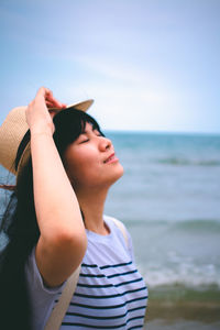 Young woman wearing hat standing at beach against sky