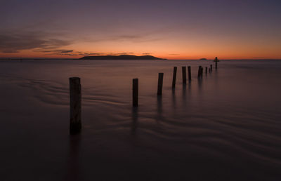 Wooden posts in sea against sky during sunset