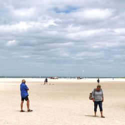 Rear view of friends walking on beach against sky