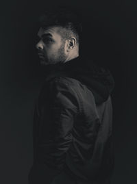 Portrait of young man standing against black background