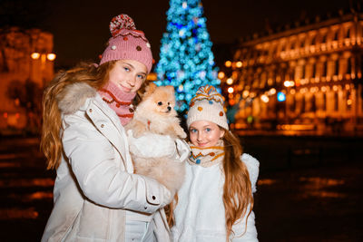 Two young girls are smiling and having fun holding spitz dog looking out