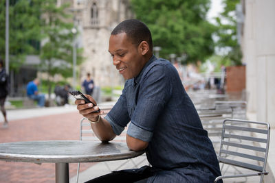 Man using mobile phone sitting on bench in city