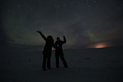 Silhouette people standing on land against sky at night during winter