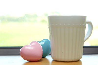 Close-up of coffee cup with heart shapes on window sill