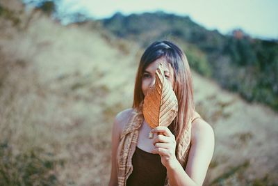 Young woman holding leaf on field