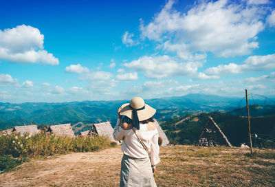 Rear view of woman standing on field against sky