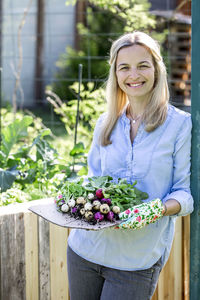 Portrait of mid adult woman holding radishes at farm