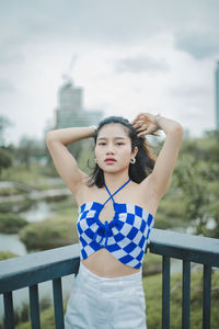 Young woman standing against railing against sky