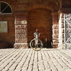Bicycle parked on cobblestone street against brick wall arch