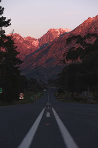 Empty road along trees and mountains against sky