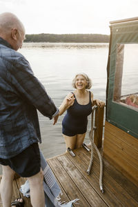 Happy senior woman in swimwear climbing houseboat by man