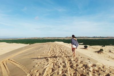 Rear view of woman walking on sandy beach against sky