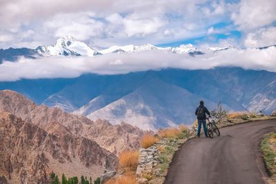 Man riding bicycle on mountain road against cloudy sky