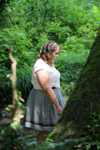 Young woman standing by trees in forest