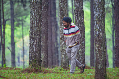 Man standing by tree trunk in forest