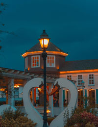 Illuminated street light by building against sky at night