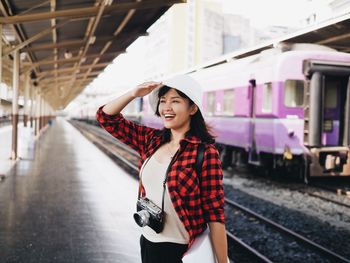 Smiling woman looking away while standing on railroad station platform