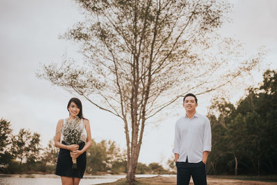 Portrait of smiling young couple standing against tree