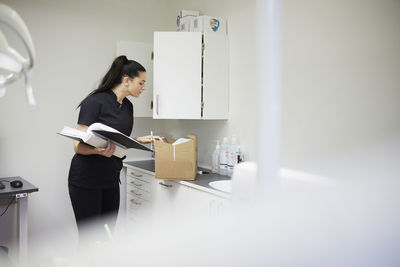 Female dentist in surgery putting supplies in cupboard