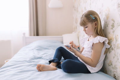 Girl looking away while sitting on bed at home
