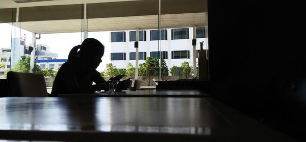 Silhouette woman sitting on table by window at home