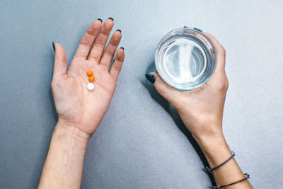 Caucasian female with two orange and one white pills in left palm and glass of water in right hand.