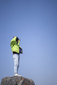 Young indian boy standing on the top of cliff wearing a snow jacket and track pants. enjoying