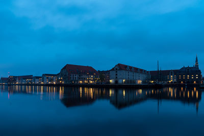 Illuminated buildings by lake against sky at night