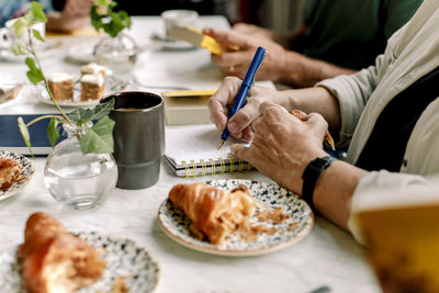 Hands of senior woman writing in diary at cafe