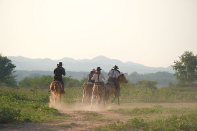 Men riding horses on landscape against sky