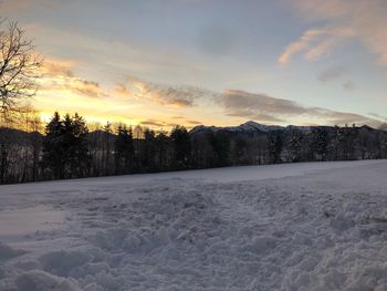 Snow covered field against sky during sunset