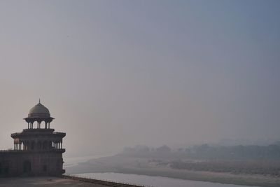 Lighthouse by sea against clear sky during sunset